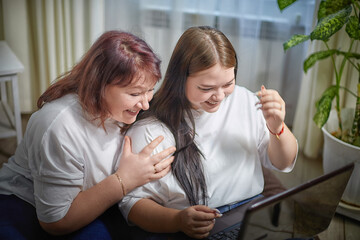 Fat funny funny adult mother and daughter with laptop indoors. A teenage girl teaches middle-aged woman modern technology. Internet, chatting