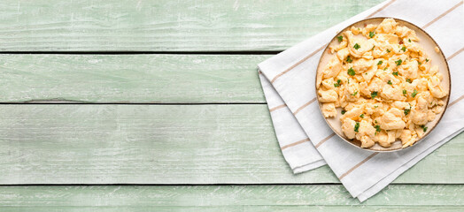Plate of scrambled eggs on napkin on green wooden table. Banner for design