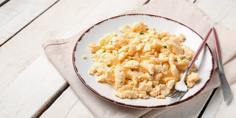 Plate of tasty scrambled eggs with cutlery on wooden table