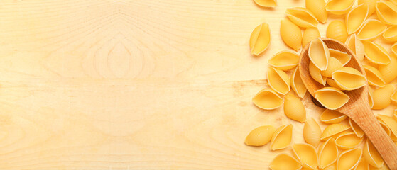 Heap of raw conchiglie pasta and spoon on wooden background with space for text