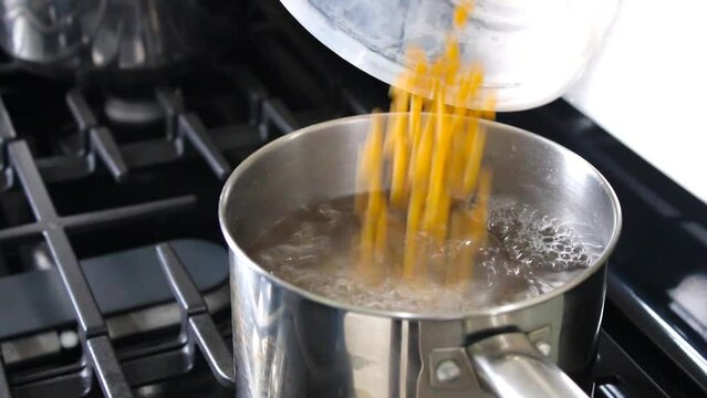 Hands adding macaroni to hot water in pot on cooking stove