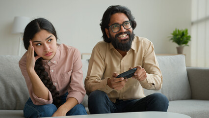 Diverse multiethnic couple at home bored angry arabian woman offend on husband addicted playing console video game with joystick focused indian man gamer ignoring wife play tv gamepad gaming addiction