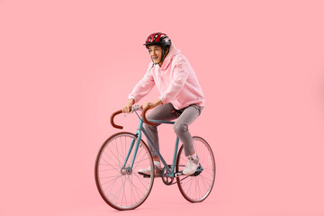 Young man in helmet riding bicycle on pink background
