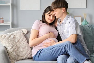 Fototapeta na wymiar Young pregnant couple sitting on sofa at home