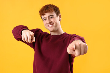 Young redhead man pointing at viewer on yellow background