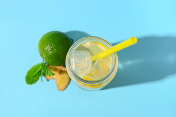 Mason jar of tasty lemonade with ginger and lime on blue background
