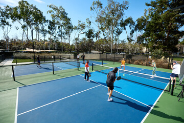 Two pickleball courts with athletes playing games with long shadows.