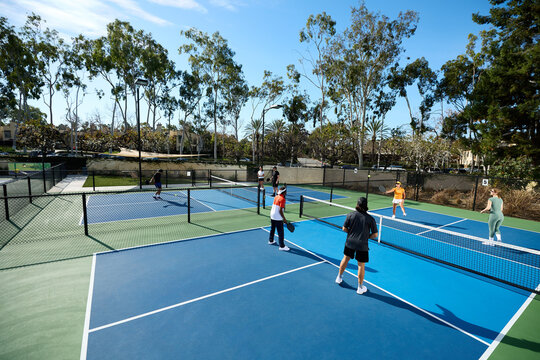 Two pickleball courts with athletes playing games with long shadows.