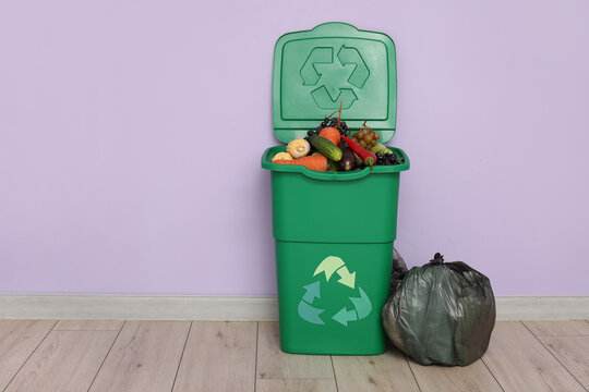 Container for trash with food waste and full garbage bags near lilac wall. Recycling concept