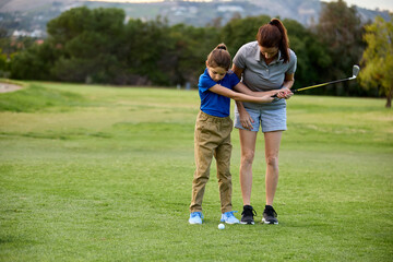 A mother helps her young daughter learn how to swing a golf club