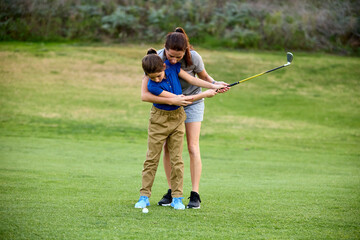 A mother helps her young daughter learn how to swing a golf club