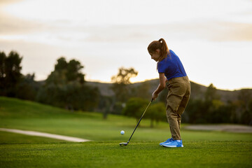 A young girl swings a golf club at sunset