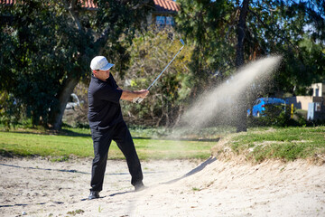 A golfer tries to get out of a sand trap