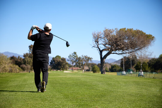 A man hits a drive off the tee box on a golf course - Powered by Adobe