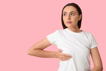 Obraz premium Young woman checking her breast on pink background. Cancer awareness concept