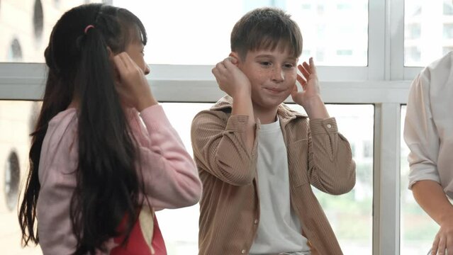 Diverse student learning about body organ while playing with teacher. Multicultural learner sitting around care taker while touching ear in STEM science class. Creative activity concept. Erudition.