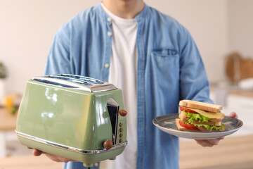 Young man with modern toaster and delicious sandwiches in kitchen, closeup