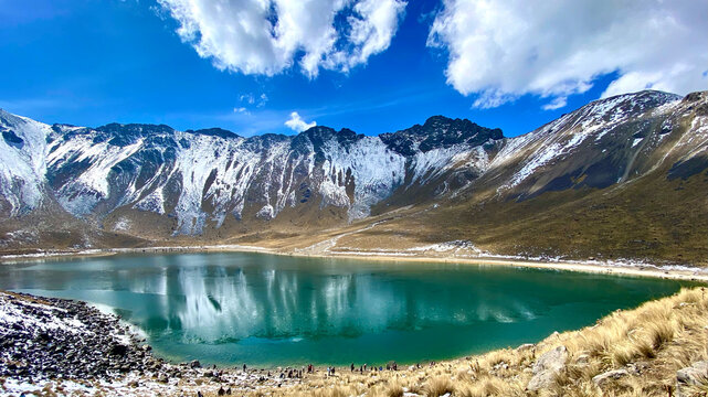 People around a frozen lake bellow snow capped mountain