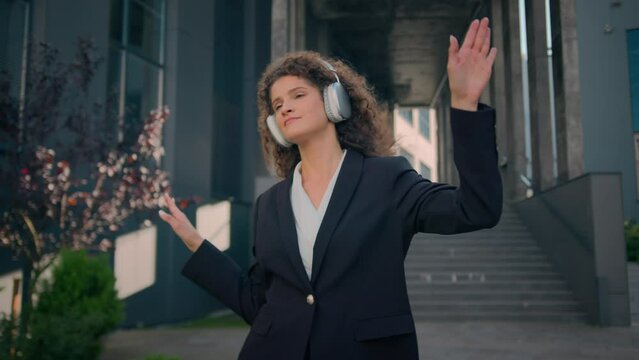 Joyful carefree girl Caucasian business woman listening music in headphones earphones on street outdoors happy businesswoman lady dancing moving listen song walking from office in city friday freedom