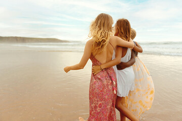 Fototapeta na wymiar multiracial group of three young women walking together embracing by the seashore. Summer trip among friends.