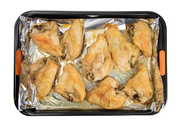 Top down view of a foil lined tray of oven baked skin on chicken breasts isolated on white