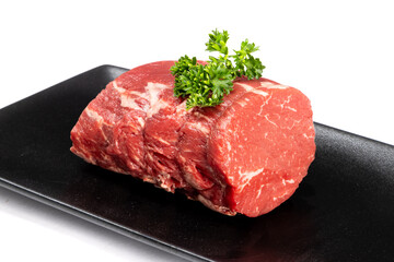A beef tenderloin roast with parsley garnish on a square black plate isolated on white
