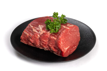 A piece of beef tenderloin roast with parsley garnish on a round black plate isolated on white
