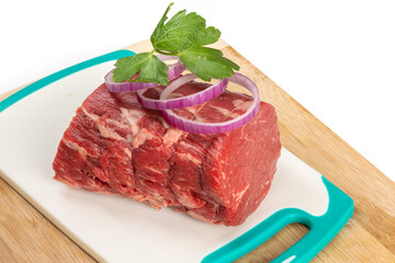 A piece of beef tenderloin roast with parsley and onion garnish on a cutting board isolated on white