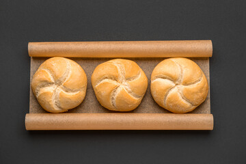 Baking paper with delicious kaiser rolls on black background