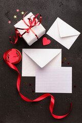 Envelopes with blank card, gift box and decor on black grunge background. Valentine's Day celebration