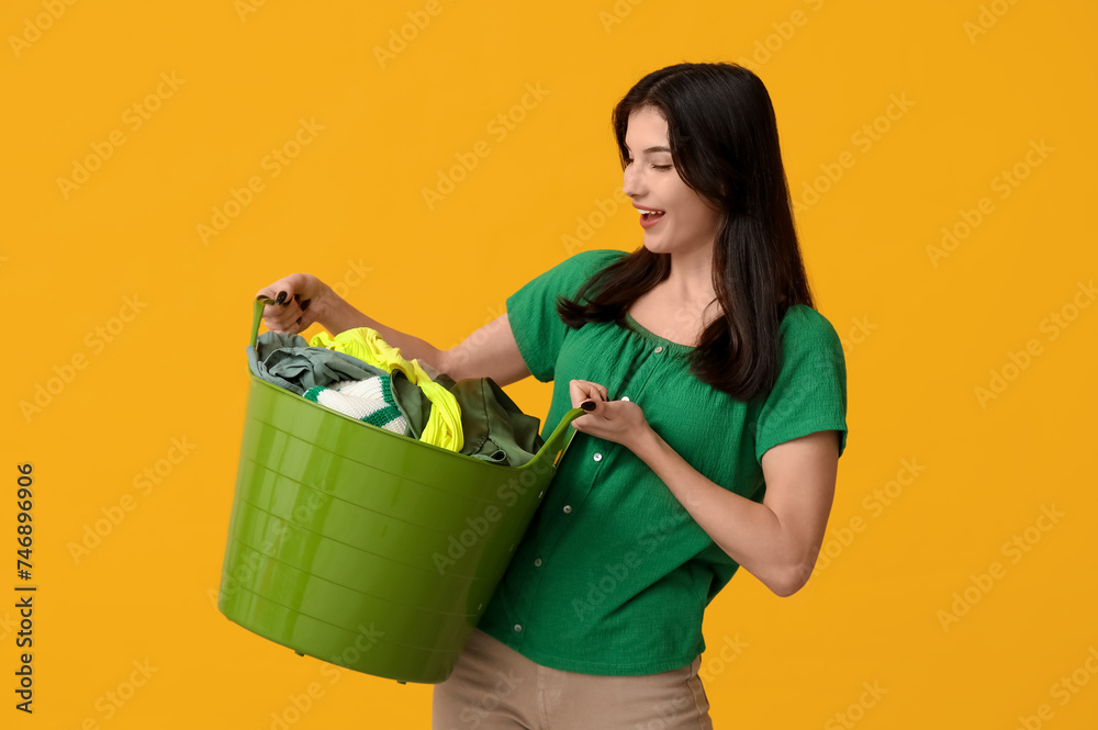 Wall mural young woman holding basket with clean laundry on yellow background