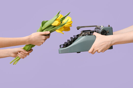 Female hands with retro typewriter and beautiful tulip flowers for International Women's Day on lilac background, closeup