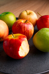 delicious apples on a plate on a wooden table, bitten apple, red apple and green apple