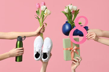 Female hands with sports equipment, shoes, gift box and tulip flowers for International Women's Day on pink background