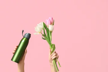 Tapeten Female hands with sports bottle of water and bouquet of tulip flowers for International Women's Day on pink background © Pixel-Shot