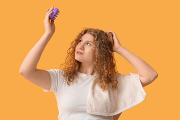 Beautiful young woman with hair scalp massager and shampoo bar on yellow background