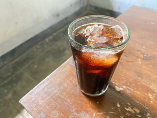 A glass of iced coffee drinks on a wooden table. Black coffee with ice cubes on the surface of the drink. Empty blank text copy space. Americano and Long Black