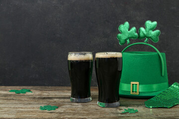 Glasses of dark beer with leprechaun hat, tie and decor for St. Patrick's Day celebration on wooden...