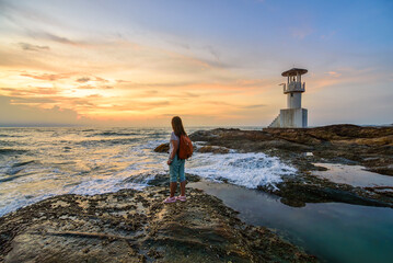 Woman backpacker solo travel alone standing on a rock with sunset sky at sea in Khao Lak Phuket Thailand. - obrazy, fototapety, plakaty