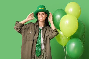 Beautiful young woman in leprechaun hat with air balloons on green background. St. Patrick's Day celebration