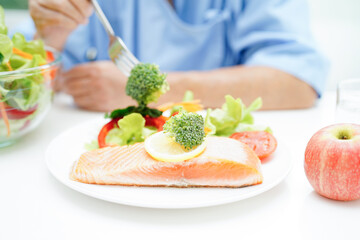 Asian elderly woman patient eating salmon stake and vegetable salad for healthy food in hospital.