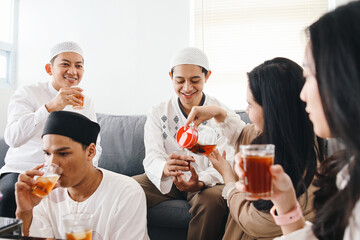 Young Asian muslim people pouring water, having iftar together at home. Break fasting concept. - obrazy, fototapety, plakaty