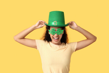 Beautiful young African-American woman in leprechaun hat and decorative glasses on yellow...