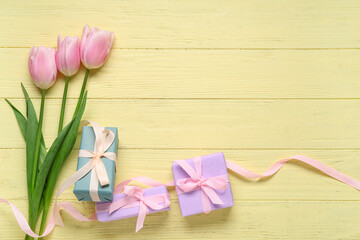 Composition with gift boxes and pink tulips on yellow wooden background. Top view