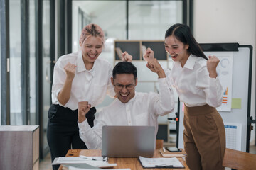 Fototapeta premium Joyful asian business team celebrating success with raised hands in office. Corporate victory and team achievement concept.