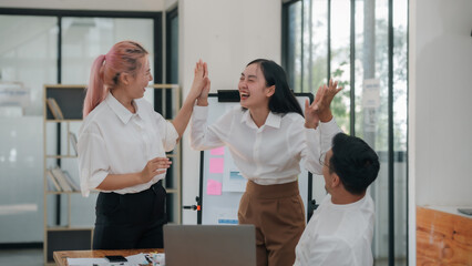Happy asian business colleagues giving high-five in office setting. Team success and partnership concept.
