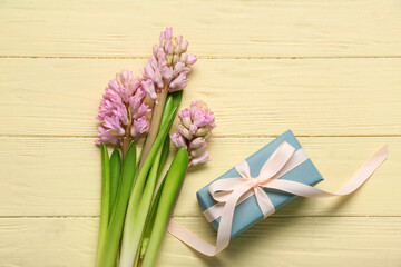 Gift box and hyacinth flower on yellow wooden background. Top view