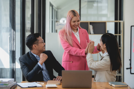 Happy asian business colleagues giving high-five in office setting. Team success and partnership concept.