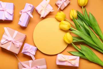 Gift boxes, yellow tulips and blank greeting card on orange background. Top view