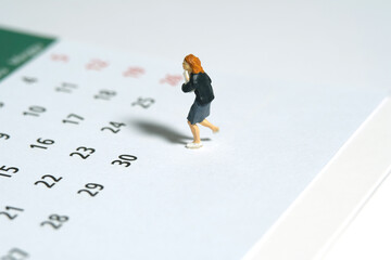 Miniature people toy figure photography. A girl pupil student running above calendar. Isolated on a...